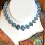 Opaque faceted aquamarine rondelles spaced with 18K gold barrel-shaped beads, shown with an orange and blue silk passim scarf