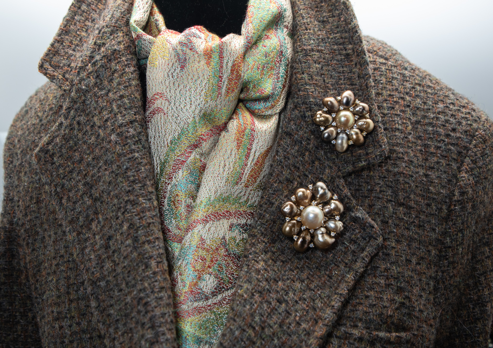 Two large Tahitian pearl brooches pinned to the lapel of a tweed blazer with silk scarf