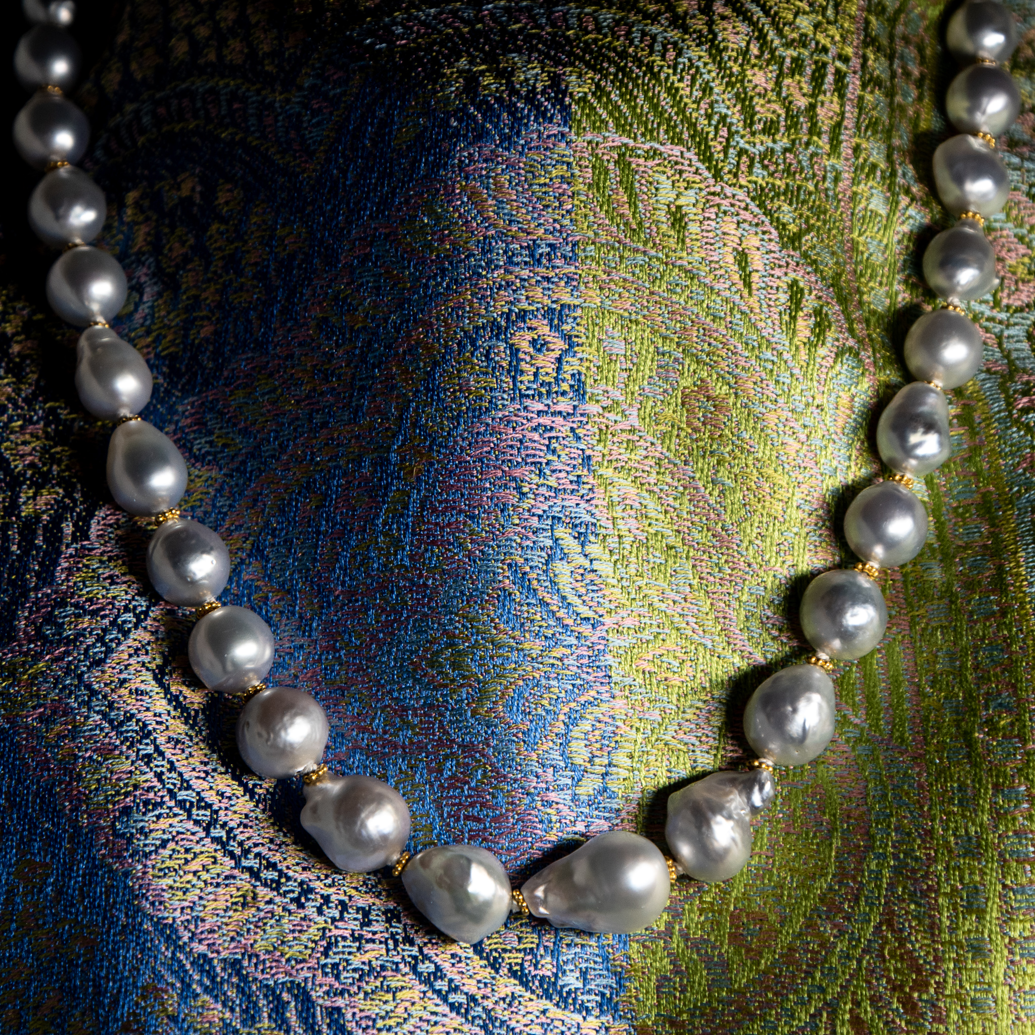 Silvery south sea pearl necklace with 22K gold accents shown on violet and chartreuse silk scarf